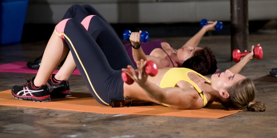 Deux femmes sont allongées au sol et font des exercices de musculation avec des altères dans les mains.