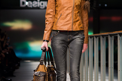 Jeune femme en blouson marron et jean, lors d'un défilé.