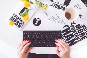 Une femme aux ongles courts et rouges tape sur clavier d'ordinateur noir.