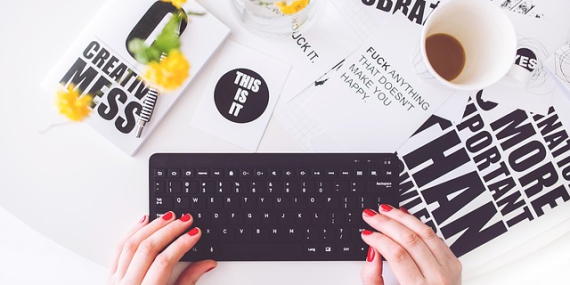 Une femme aux ongles courts et rouges tape sur clavier d'ordinateur noir.