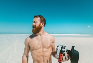 Photographie d'un homme torse nu sur une plage paradisiaque.