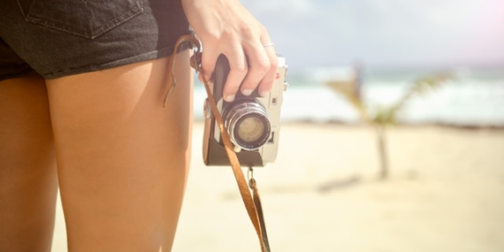 Les jambes d'une femme et sa main qui tient un appareil photo sur un fond paradisiaque.